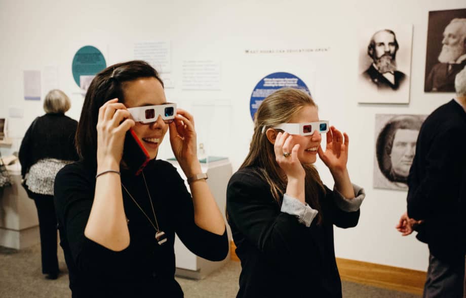 Two young women wearing 3D glasses and looking at an exhibit.