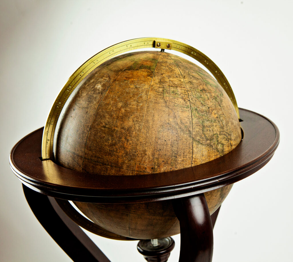 This is a globe of the world. In a brass ring set into a wooden stand with three legs. Surface of globe has yellowed and is crcked in several places.